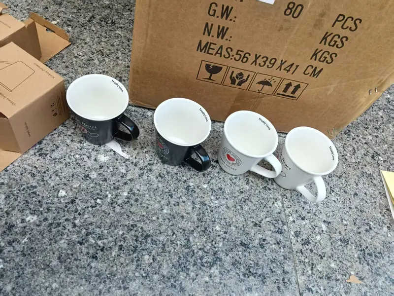 Four mugs in front of a carton marked with gross weight, net weight and dimensions