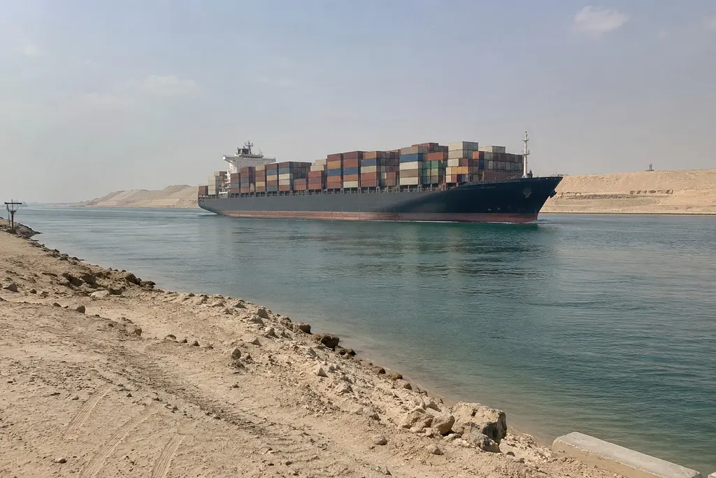 Loaded container ship sailing through a canal between sandy desert banks